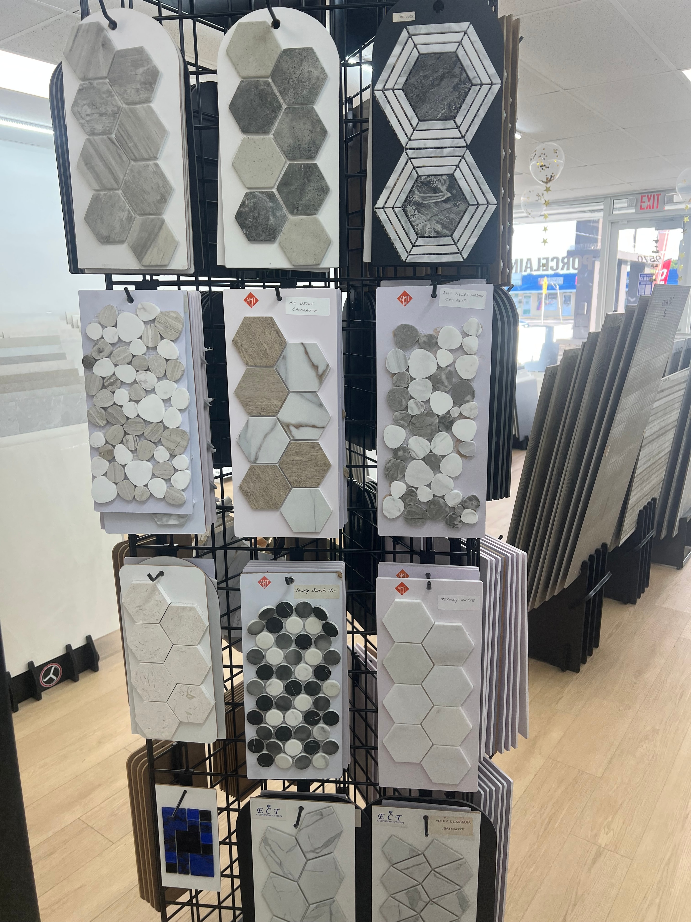 Rack del showroom con mosaicos hexagonales, penny round y geométricos en mármol blanco, gris y negro